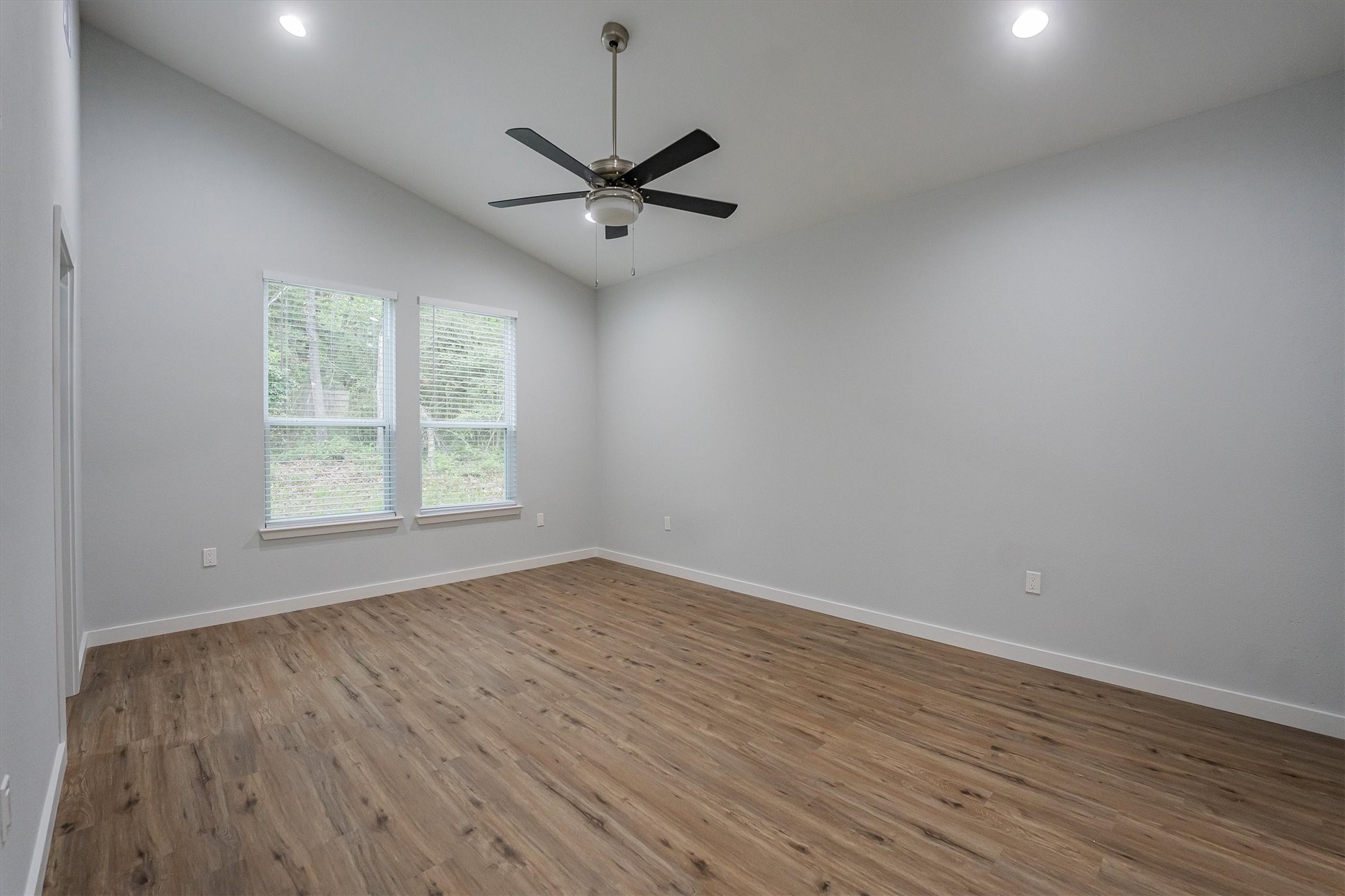 24411 Oakaland Hls Road Point Blank, TX 77364 - Photo 24 of 40 an empty room with wooden floor chandelier fan and windows