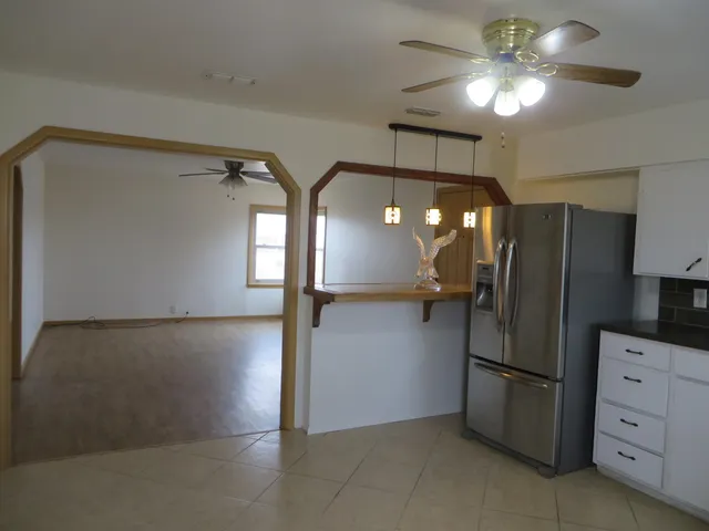 a view of a refrigerator in kitchen and an empty room with wooden floor