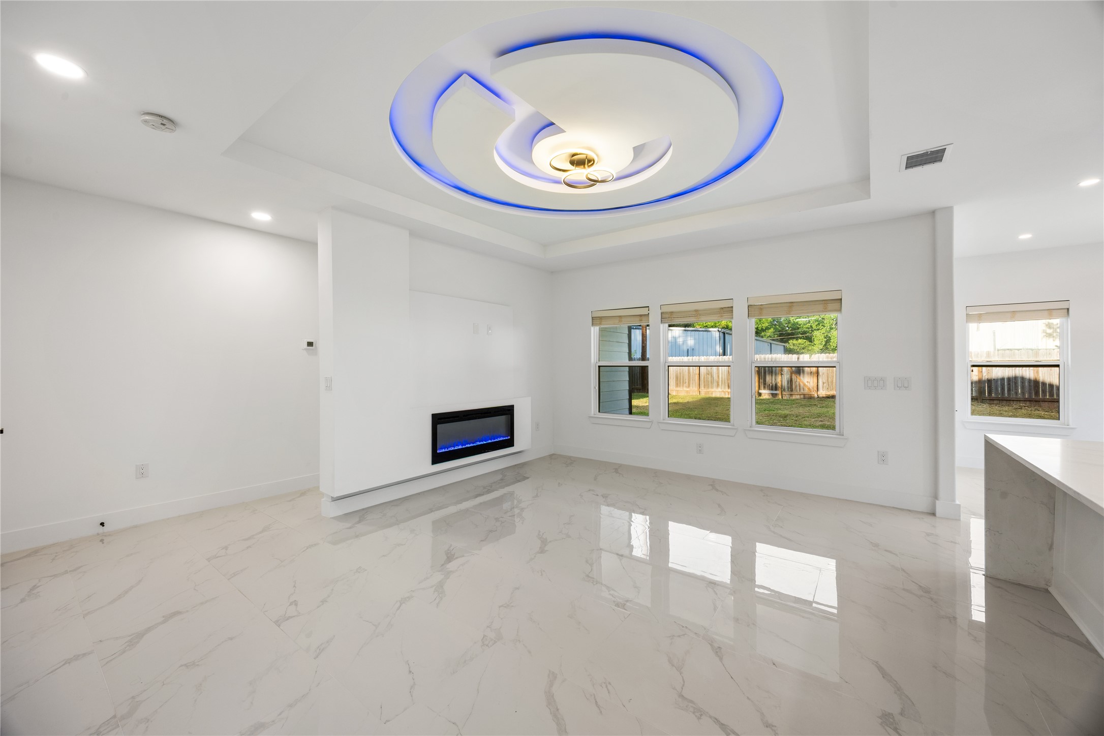 1121 Austin Street Rosenberg, TX 77471 - Photo 24 of 44 This modern living space features sleek white large format porcelain floors, a contemporary electric fireplace, and a striking ceiling design with blue LED lighting. Large windows offer ample natural light and a view of the backyard.