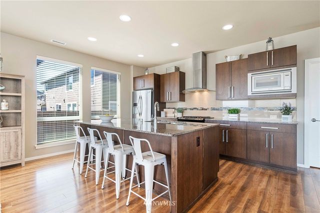 a kitchen with stainless steel appliances granite countertop a stove top oven a sink dishwasher and white cabinets with wooden floor