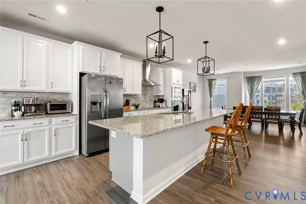 a kitchen with stainless steel appliances granite countertop a stove a refrigerator a kitchen island a dining table and chairs with wooden floor