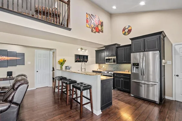 a kitchen with stainless steel appliances granite countertop a refrigerator a stove a sink and chairs with wooden floor