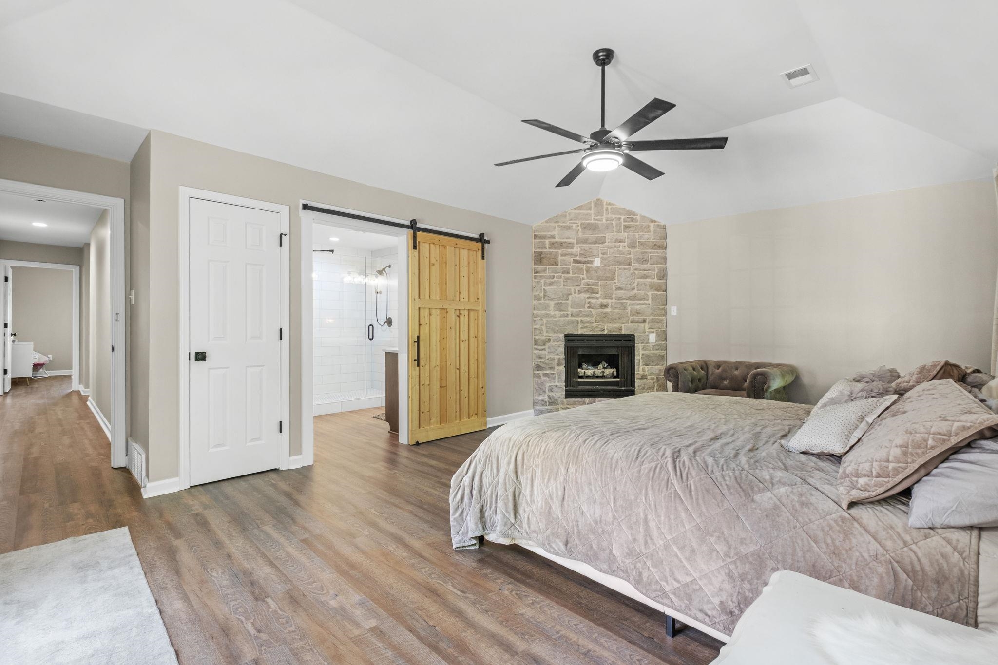 650 Firetower Road Somerville, TN 38068 - Photo 18 of 39 Bedroom with a barn door, vaulted ceiling, wood finished floors, connected bathroom, and a stone fireplace