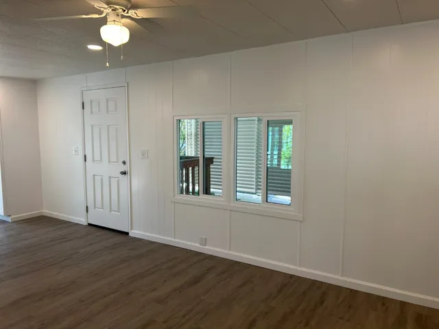an empty room with wooden floor fan and windows
