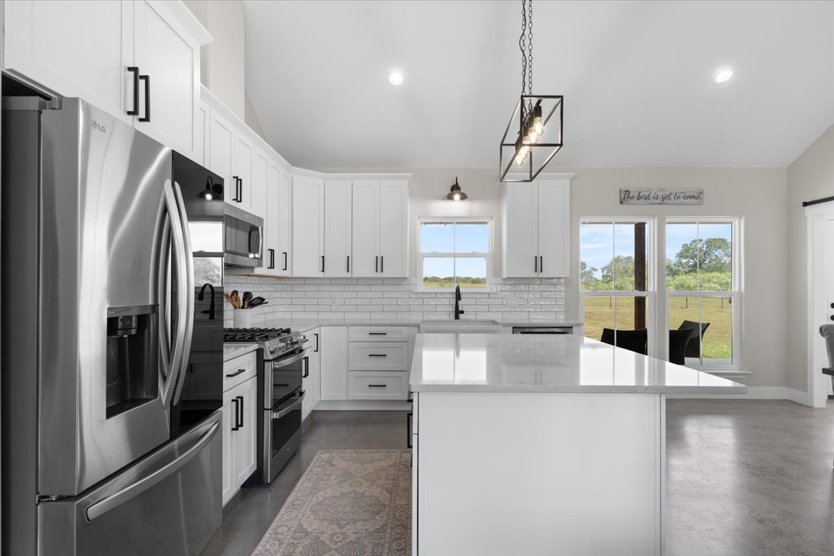 3389 Sparta Field Road Waelder, TX 78959 - Photo 8 of 40 Kitchen featuring appliances with stainless steel finishes, vaulted ceiling, decorative backsplash, a center island, and finished concrete flooring
