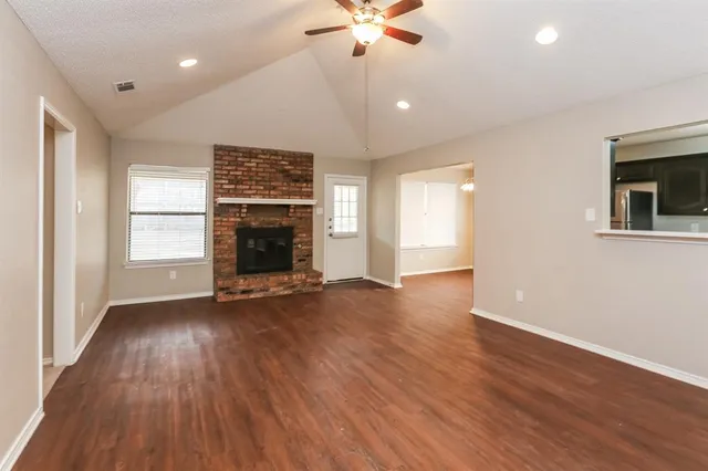an empty room with wooden floor fireplace and windows
