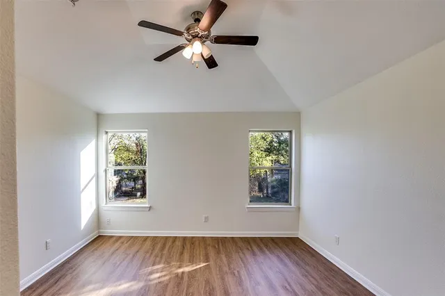 an empty room with wooden floor chandelier fan and windows