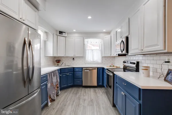 a kitchen with stainless steel appliances granite countertop a refrigerator a sink dishwasher a stove and white cabinets with wooden floor