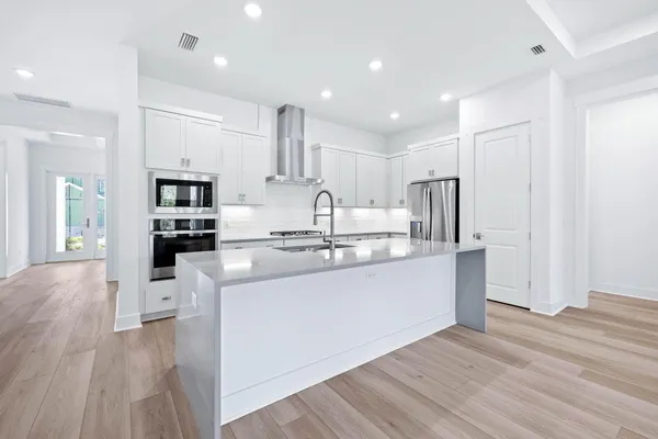 a kitchen with stainless steel appliances granite countertop a refrigerator oven a sink dishwasher and white cabinets with wooden floor