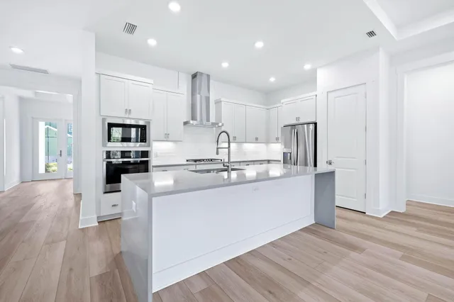 a kitchen with stainless steel appliances granite countertop a refrigerator oven a sink dishwasher and white cabinets with wooden floor