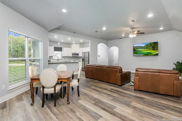 a living room with furniture a dining table wooden floor and a large window