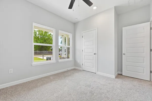 an empty room with chandelier fan and windows