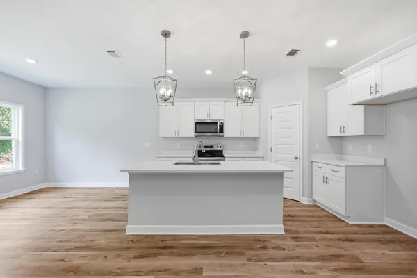 a large kitchen with granite countertop a stove a sink a center island and wooden floor
