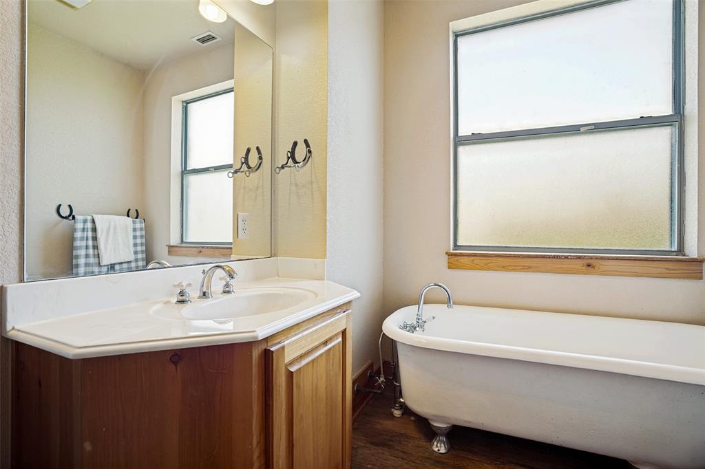 243 ROCK Court Decatur, TX 76234 - Photo 13 of 25 Bathroom featuring a clawfoot tub, wood-finish flooring, a single-basin vanity with an integrated sink, a large mirror, and a frosted window