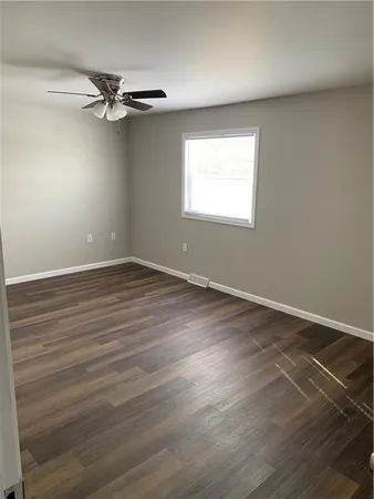 an empty room with wooden floor fan and windows
