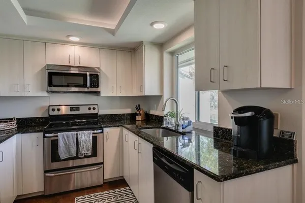 a kitchen with granite countertop a sink dishwasher a stove and a microwave oven with cabinets