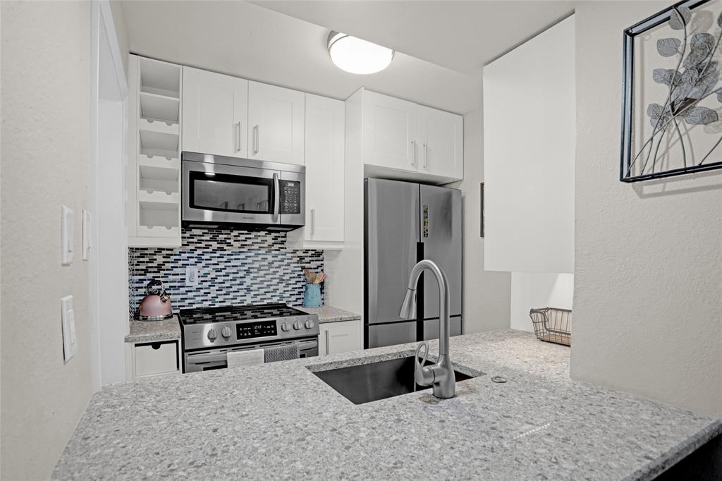 12834 Midway Road, Unit 2110 Dallas, TX 75244 - Photo 1 of 1 Kitchen with white cabinetry, light stone counters, stainless steel appliances, a textured wall, and a peninsula