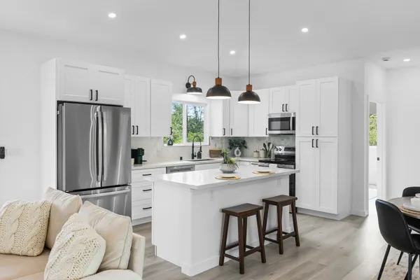 a kitchen with stainless steel appliances kitchen island granite countertop a refrigerator a stove a sink and a dining table with wooden floor