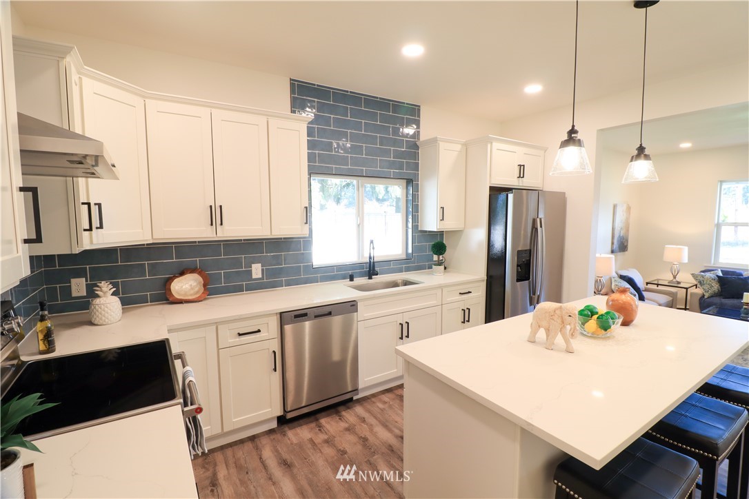 9331 Cullens Road Southeast Yelm, WA 98597 - Photo 9 of 28 a kitchen with stainless steel appliances a sink dishwasher a refrigerator a stove a dining table and chairs with wooden floor