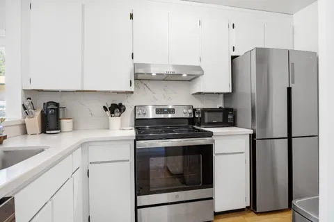 a kitchen with stainless steel appliances granite countertop a refrigerator a stove a sink and white cabinets