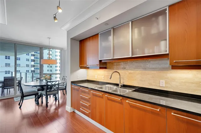 a kitchen with stainless steel appliances granite countertop a stove top oven a sink a dining table and chairs with wooden floor