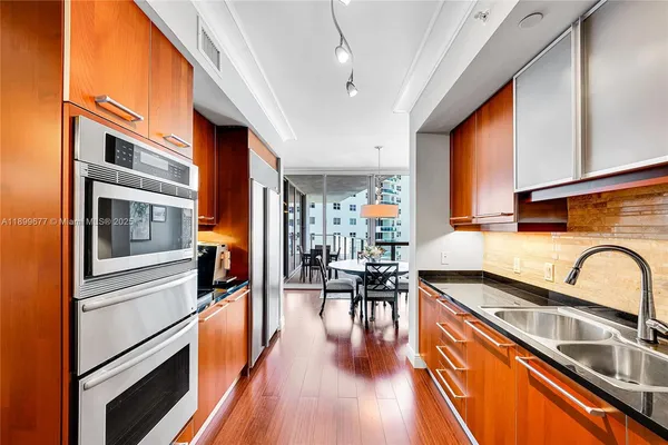 a kitchen with stainless steel appliances granite countertop a refrigerator a stove and a sink with wooden floor