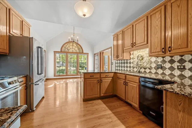 a kitchen with stainless steel appliances granite countertop a stove a sink dishwasher and a refrigerator with wooden floor