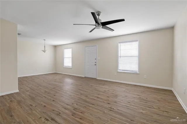 an empty room with wooden floor fan and windows