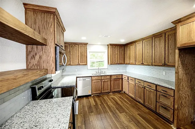 a kitchen with granite countertop a sink dishwasher stove and white cabinets with wooden floor
