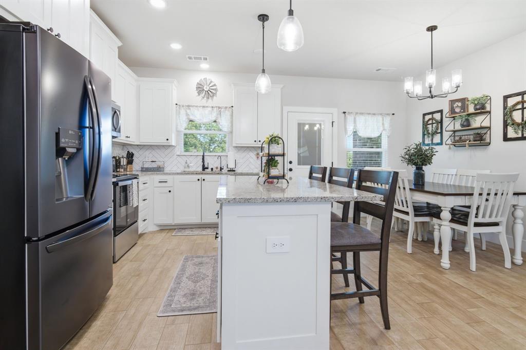 112 Monarch Lane Poolville, TX 76487 - Photo 13 of 37 Open-concept kitchen and dining area featuring white shaker cabinetry, light-toned wood-finish flooring, a kitchen island with a stone countertop, a tile backsplash, and recessed and pendant lighting