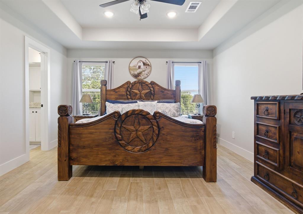 112 Monarch Lane Poolville, TX 76487 - Photo 17 of 37 Spacious bedroom featuring wood-finish flooring, a tray ceiling with recessed lighting and a ceiling fan, and two windows providing natural light