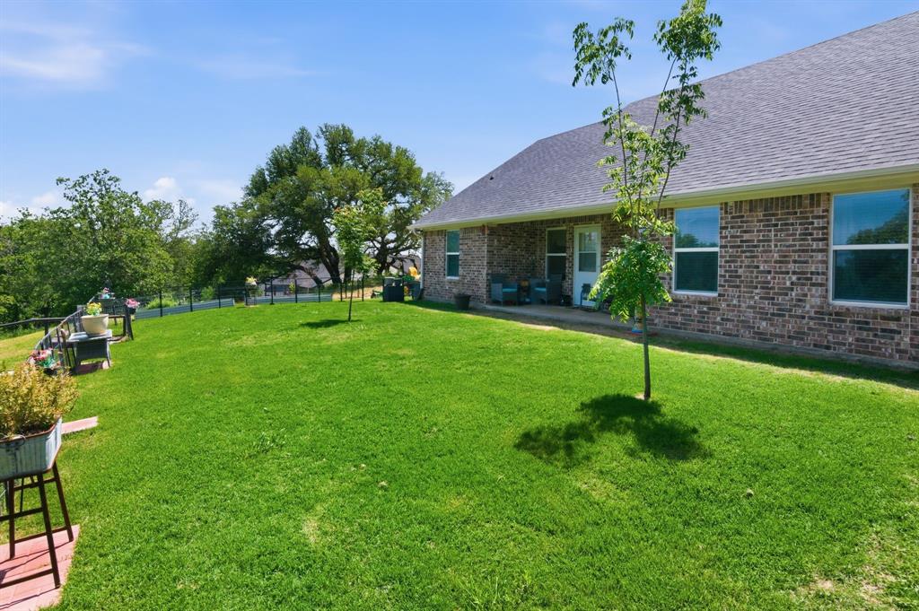 112 Monarch Lane Poolville, TX 76487 - Photo 30 of 37 Spacious backyard featuring a manicured lawn, a low-profile fence, and mature trees