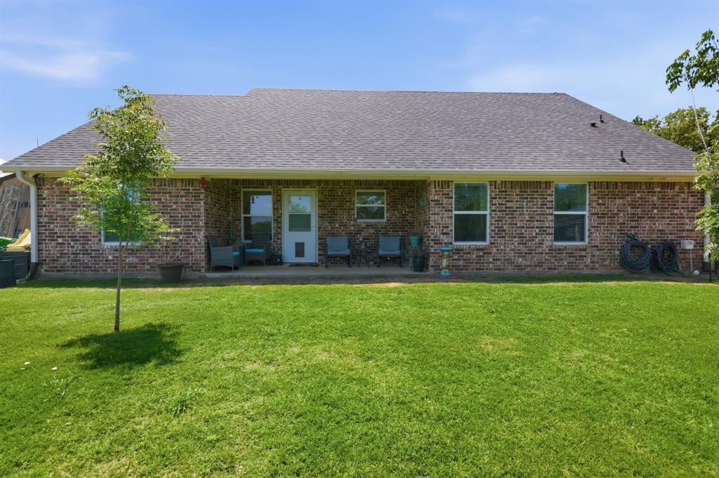 112 Monarch Lane Poolville, TX 76487 - Photo 33 of 37 Expansive green lawn with a brick exterior home featuring multiple windows, a covered patio, and a screen door
