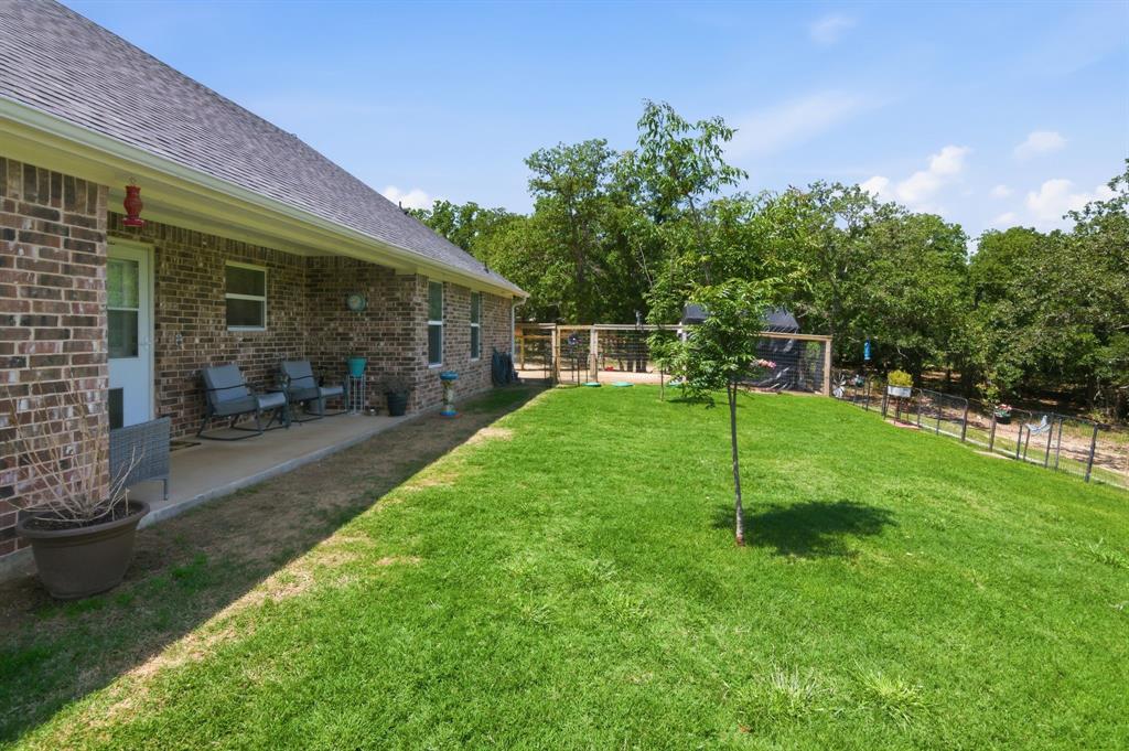 112 Monarch Lane Poolville, TX 76487 - Photo 34 of 37 Expansive backyard featuring a brick exterior with a covered patio, a manicured lawn, and a fenced area