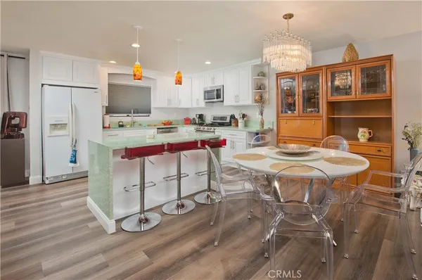a open kitchen with stainless steel appliances kitchen island granite countertop a stove a refrigerator a sink a dining table and chairs with wooden floor