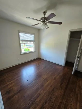 an empty room with wooden floor fan and windows