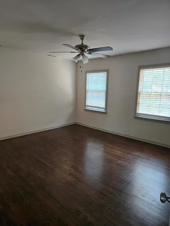 an empty room with wooden floor fan and windows