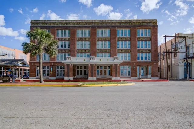 a front view of a building with small garden and trees