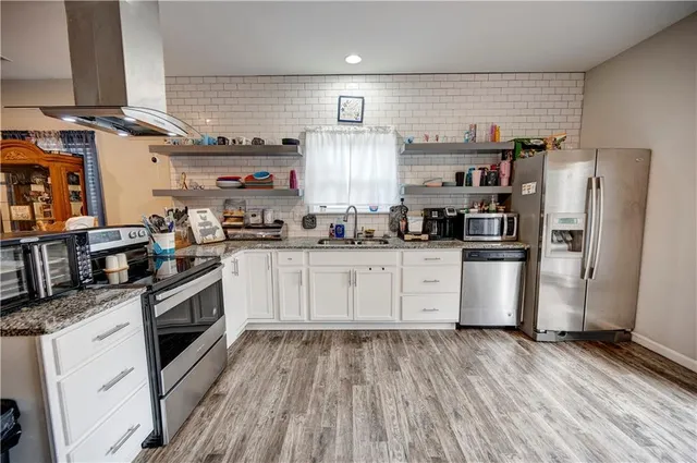 a kitchen with stainless steel appliances kitchen island granite countertop a refrigerator a sink dishwasher a stove and white cabinets with wooden floor