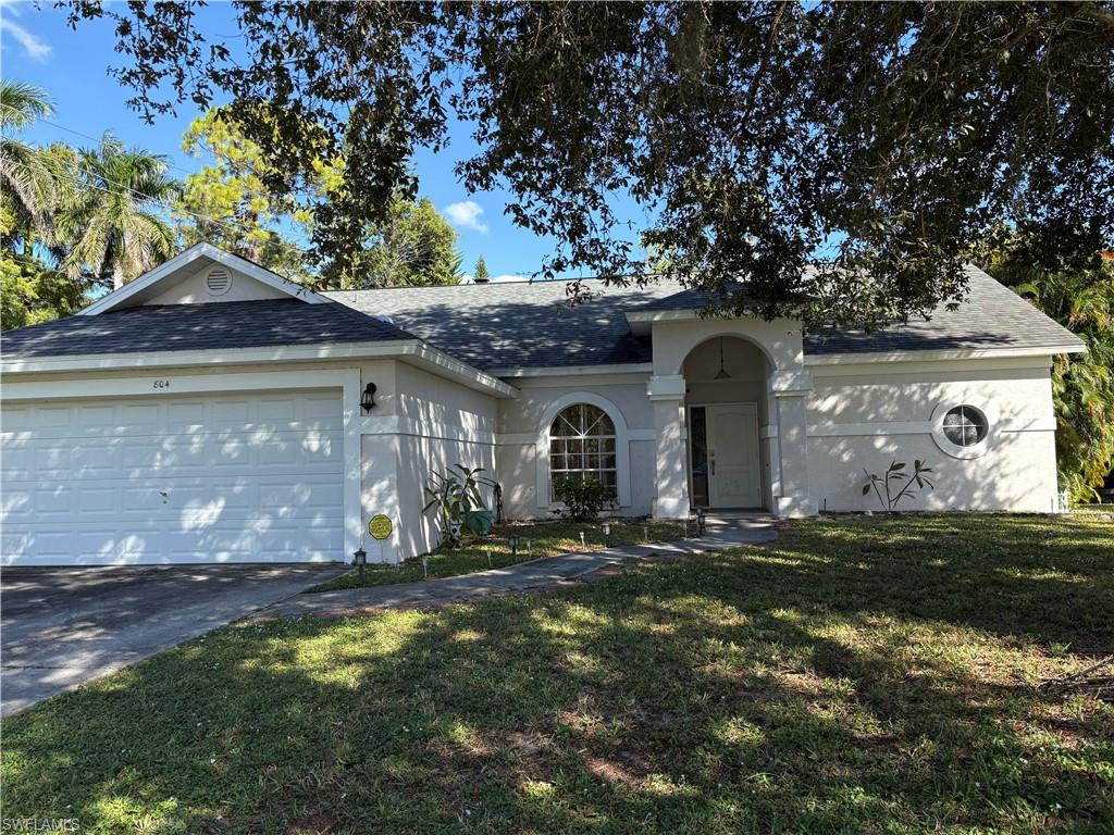 804 Bluebird Street Naples, FL 34104 - Photo 12 of 42 View of front facade featuring roof with shingles, a front lawn, concrete driveway, stucco siding, and an attached garage