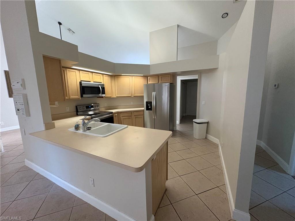 804 Bluebird Street Naples, FL 34104 - Photo 5 of 42 Kitchen featuring light countertops, light tile patterned floors, a high ceiling, appliances with stainless steel finishes, and a peninsula