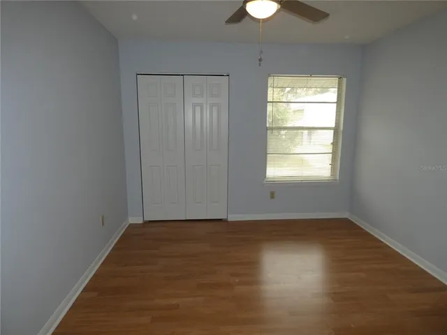 an empty room with wooden floor chandelier fan and windows