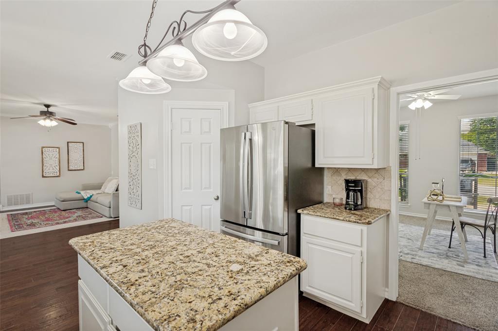 1228 Concho Drive Benbrook, TX 76126 - Photo 17 of 39 Kitchen island with granite countertop, white cabinetry, and a stainless steel refrigerator