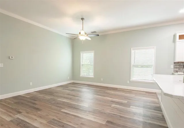an empty room with wooden floor fan and windows
