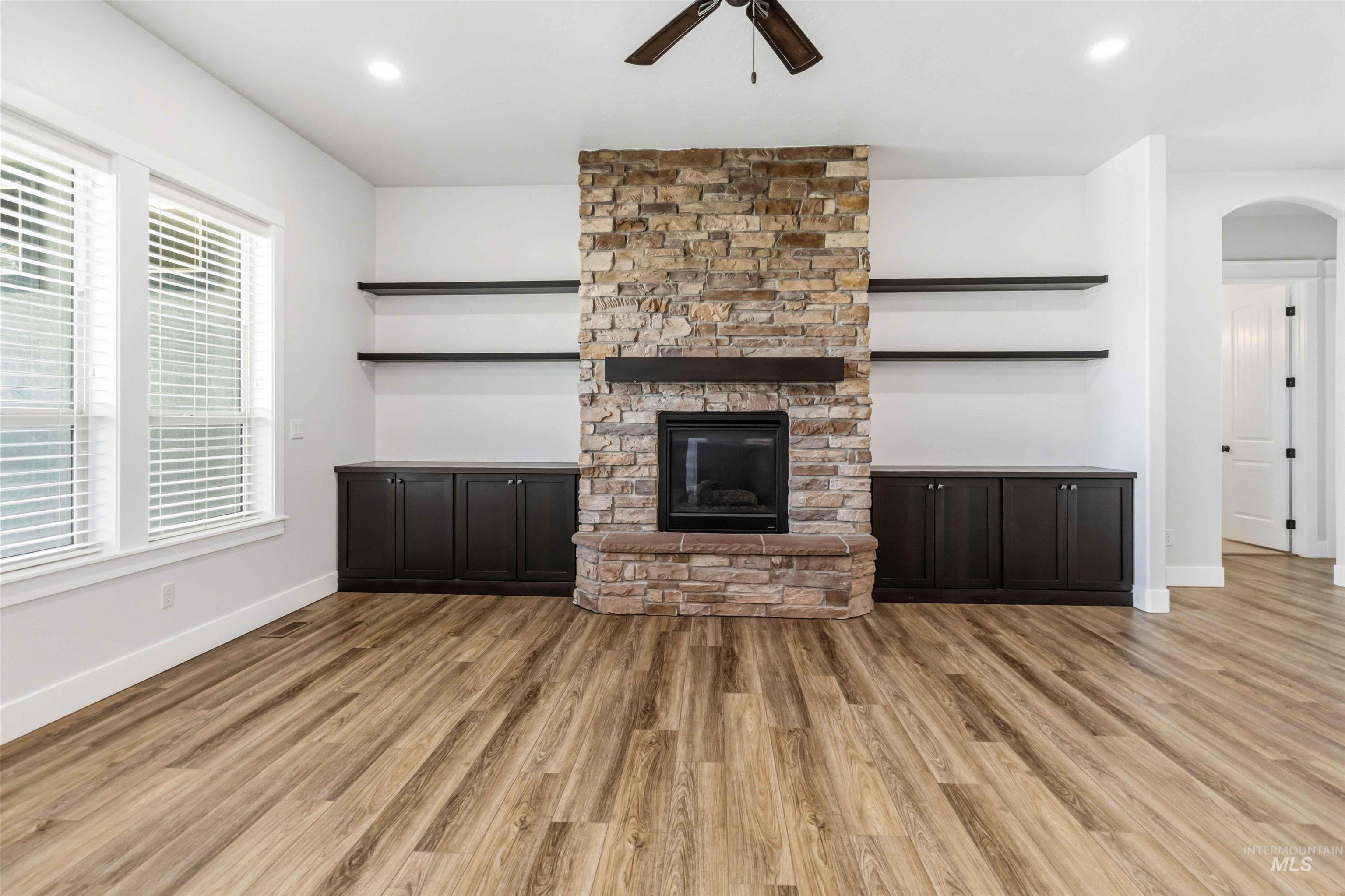3218 North Cherry Laurel Way Star, ID 83669 - Photo 10 of 50 Open concept living area featuring wood-finish flooring, a stone fireplace with a dark wood mantel, built-in shelving, and a ceiling fan