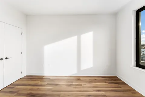 a view of an empty room with wooden floor and a window