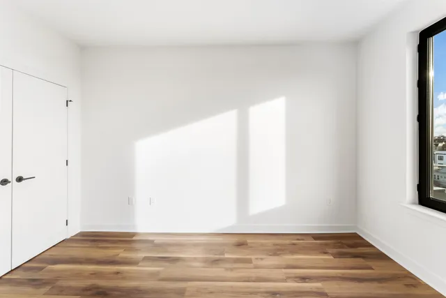 a view of an empty room with wooden floor and a window