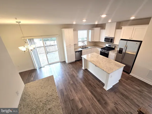 a living room with stainless steel appliances furniture wooden floor and a kitchen view