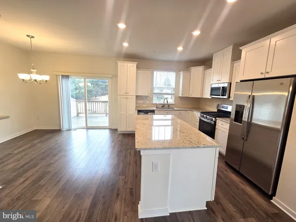 a kitchen with stainless steel appliances granite countertop a refrigerator a sink dishwasher a stove and white countertops with wooden floor