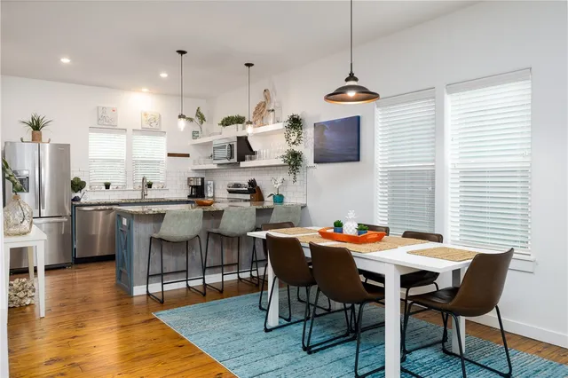 a dining room with stainless steel appliances kitchen island a table chairs and a wooden floor